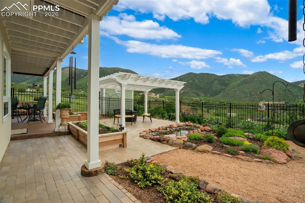 Image 32 of 40: Fully landscaped back yard with stone patio, pergola, and pond
