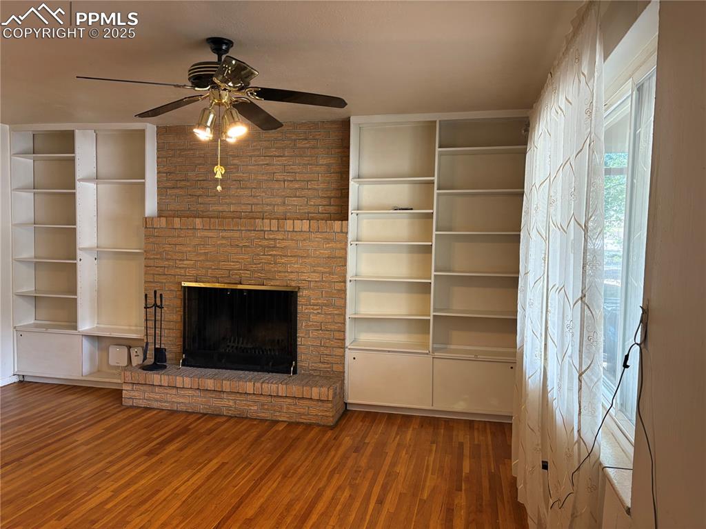 Image 5 of 11: Unfurnished living room featuring a fireplace, built in features, wood fini