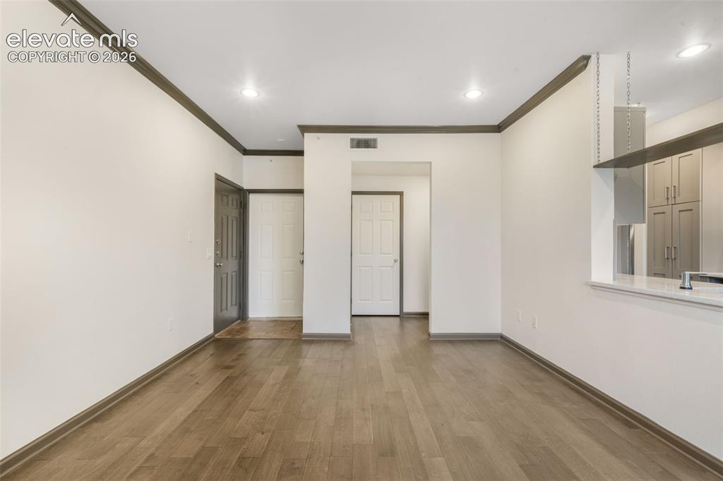Image 11 of 50: Wood-finish flooring, recessed lighting, crown molding, and pass-through co