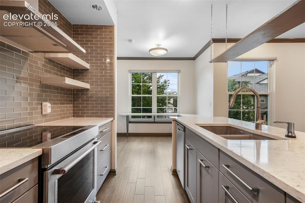 Image 15 of 50: Kitchen featuring grey cabinetry, light-toned stone countertops, a brick-pa