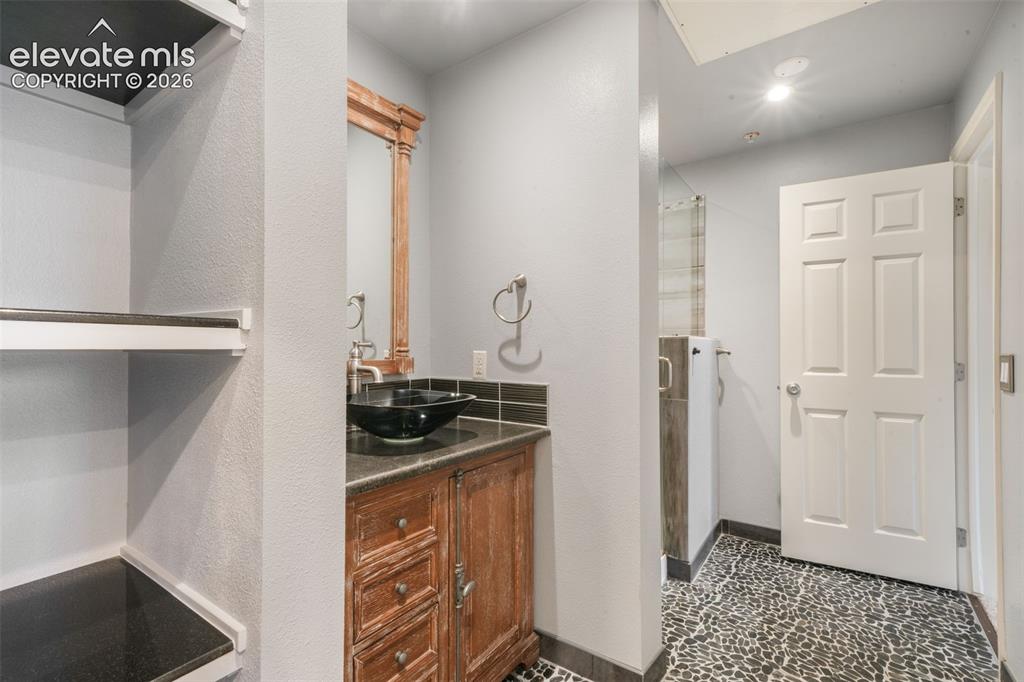 Image 27 of 50: Bathroom vanity featuring a dark stone countertop, an integrated black vess