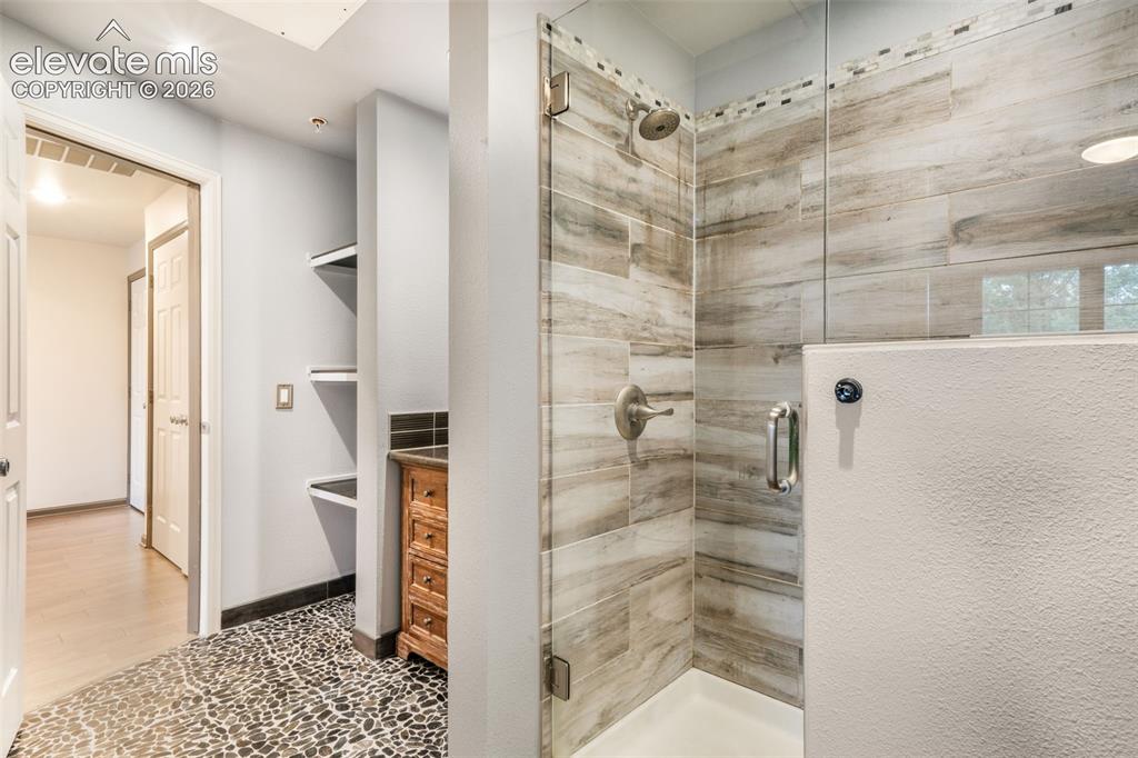 Image 29 of 50: Walk-in shower featuring wood-finish tile surround, pebble-style floor tili