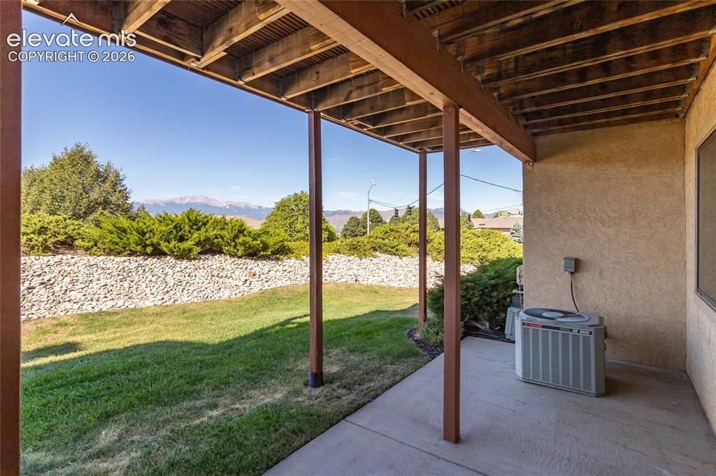Image 14 of 29: Covered patio with concrete flooring, wood beam ceiling, and mountain backd