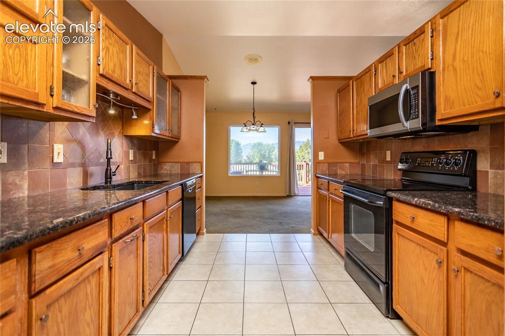Image 21 of 29: Kitchen featuring wood cabinetry, dark countertops, tile flooring, and inte