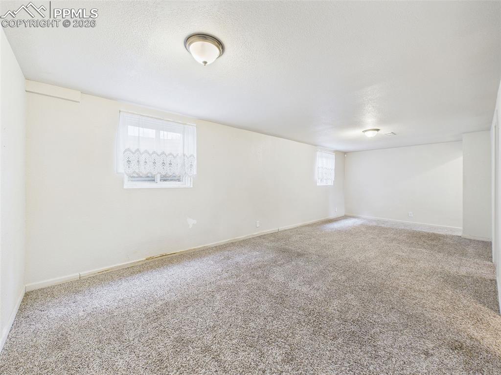 Image 32 of 50: A large, open basement family room with plush carpeting and neutral walls—i
