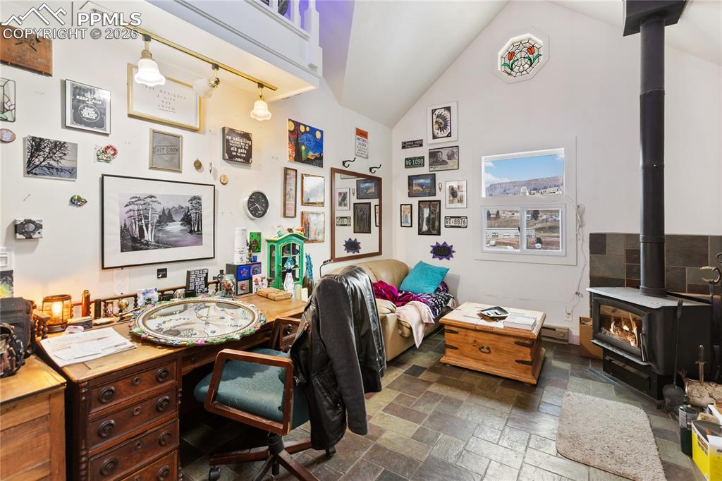Image 8 of 34: The living area has stone tile floors, a wood stove, lofted ceilings, and a