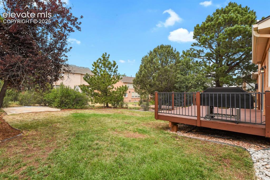 Image 43 of 50: Wood-tone deck with black metal railing, offering direct access to the gras