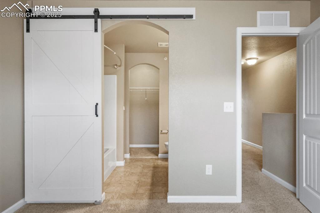 Image 13 of 18: Primary bathroom with arched walkways and a barn door
