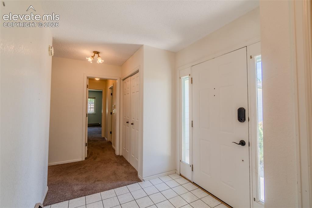 Image 11 of 47: White paneled entry door with sidelight windows, tile flooring, and a hallw