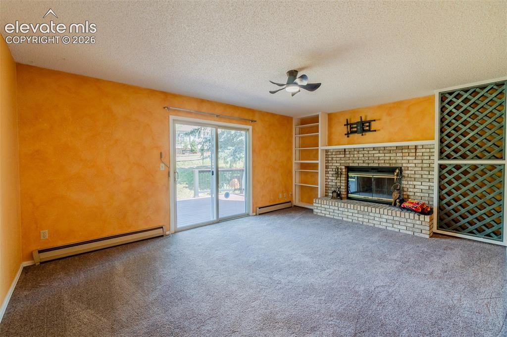 Image 14 of 47: Spacious room featuring a brick-surround fireplace, built-in shelving, glas