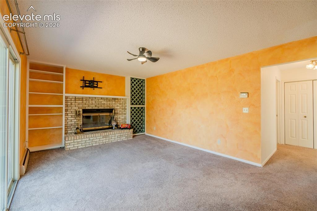 Image 15 of 47: Built-in shelving, brick fireplace with a hearth, ceiling fan, and sliding 