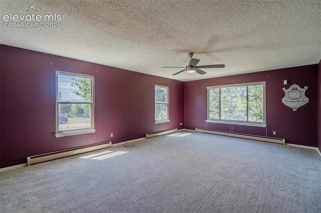 Image 20 of 47: Spacious room with multiple windows, textured ceiling, ceiling fan, and bas