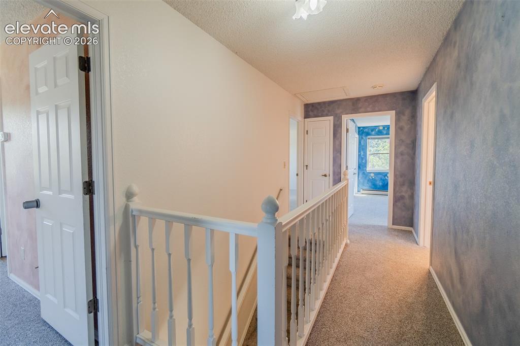 Image 27 of 47: Carpeted hallway with white interior doors, a white banister, cool paint an