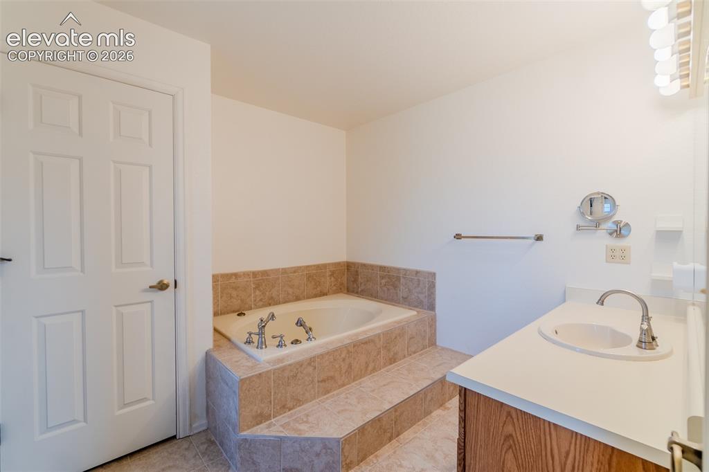 Image 41 of 47: Built-in jetted tub with tile surround, wood-finish vanity with countertop 