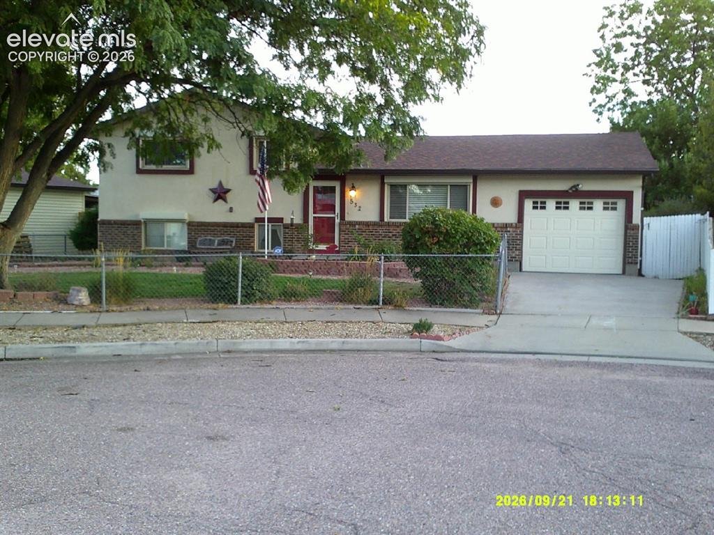 Caption: Front exterior featuring a chain link fence, concrete driveway, attached garage, and a red front doo