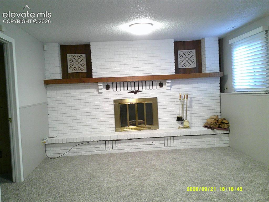 Image 12 of 26: Expansive white brick fireplace with a brass firebox, a wood mantel, and in