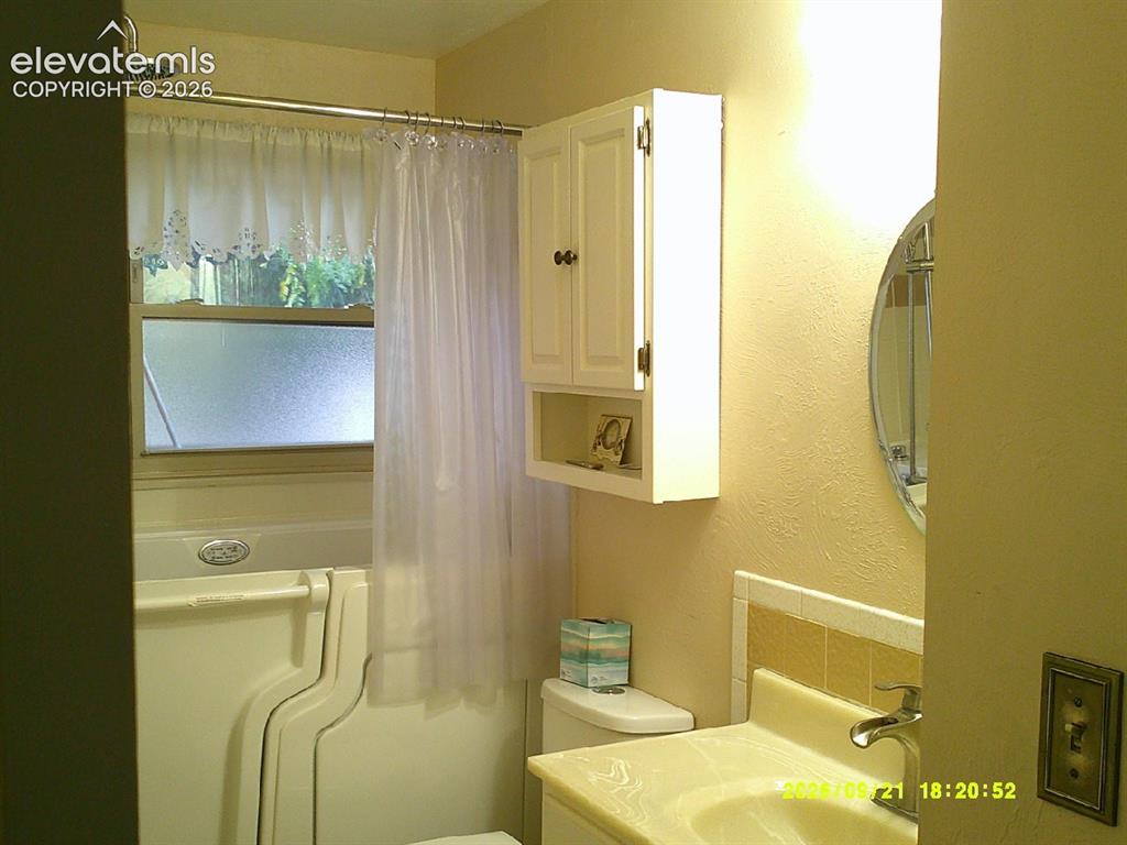 Image 19 of 26: Wall-mounted medicine cabinet with open shelving, circular wall mirror, and