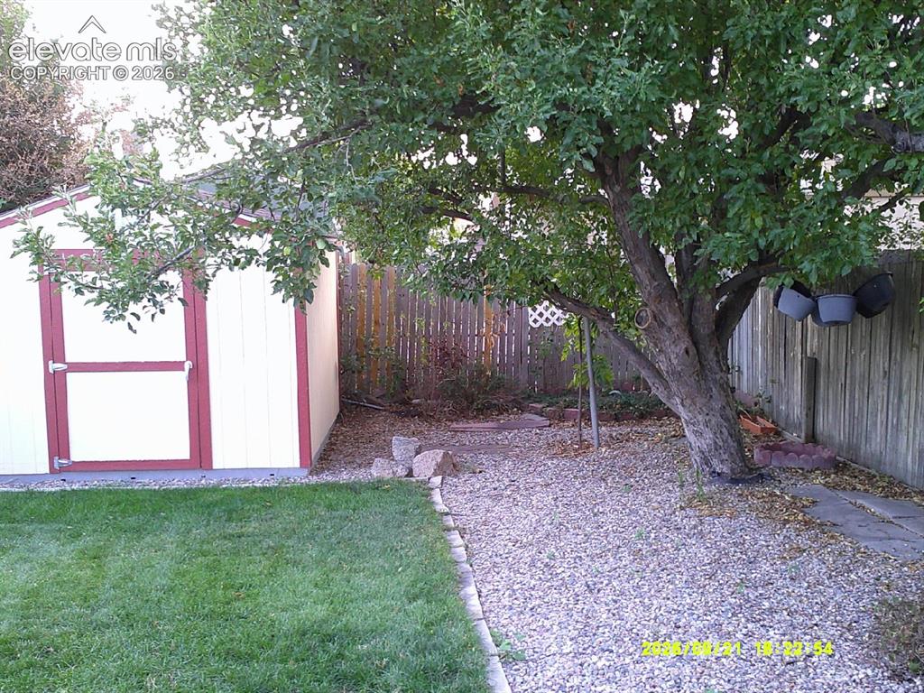 Image 21 of 26: Expansive backyard featuring a manicured lawn, established shade tree, grav