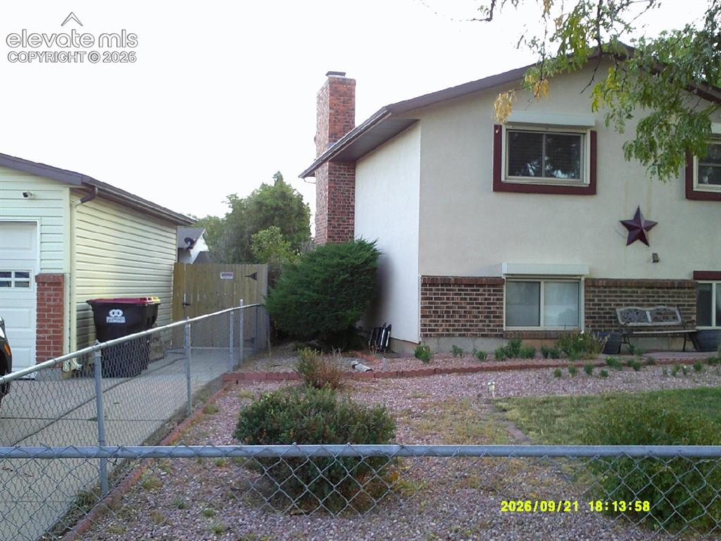 Image 3 of 26: Stucco exterior with brick detailing, attached garage, and a chain-link fen
