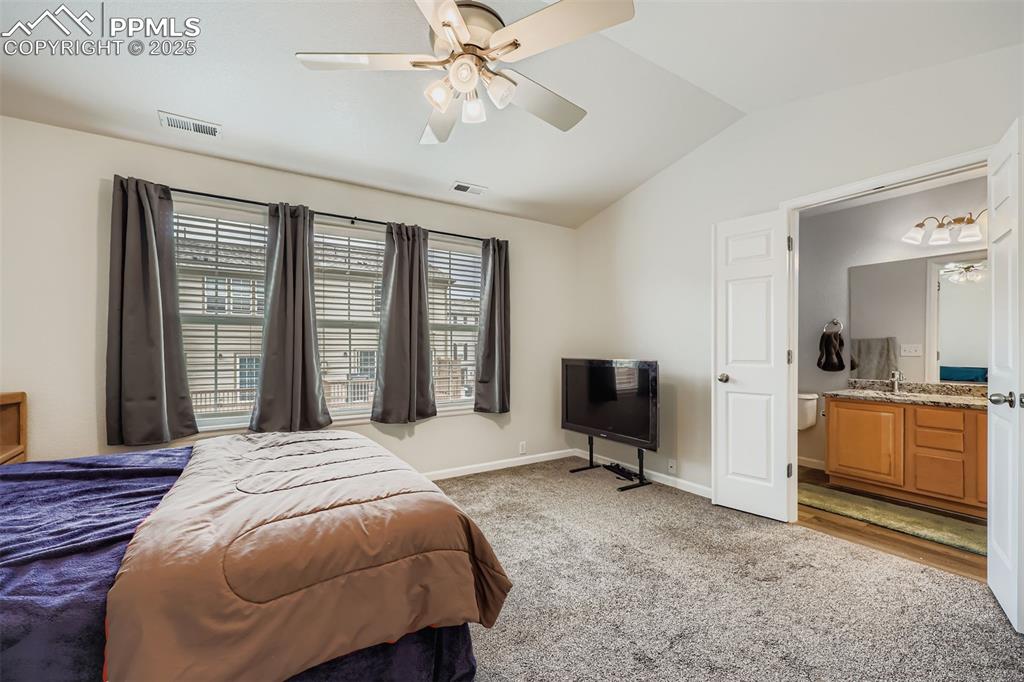 Image 16 of 27: Bedroom with light carpet, vaulted ceiling, a ceiling fan, and connected ba
