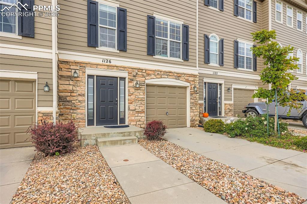 Image 2 of 27: Property entrance featuring stone siding, a garage, and driveway