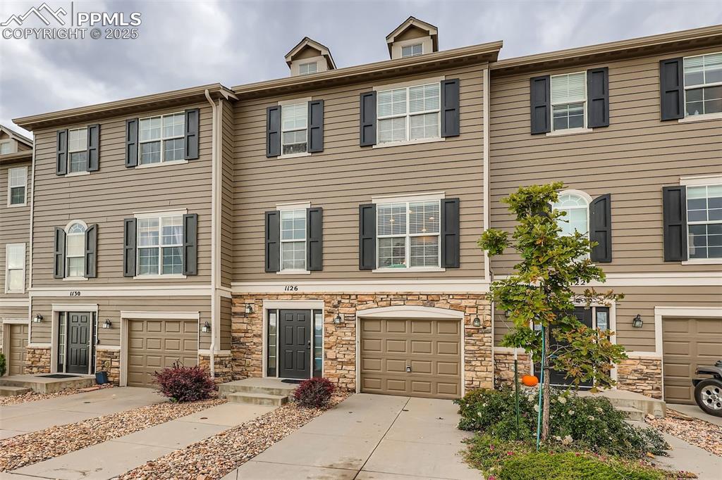 Image 27 of 27: View of front of property with concrete driveway, stone siding, and a garag