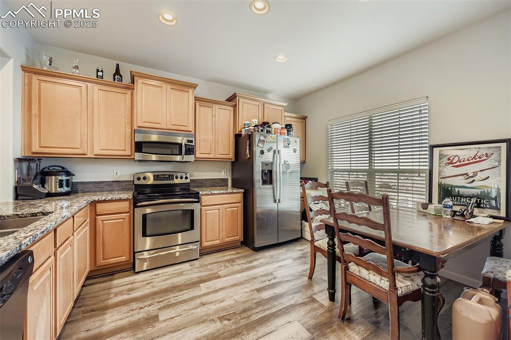 Image 5 of 27: Kitchen with light stone countertops, stainless steel appliances, light bro