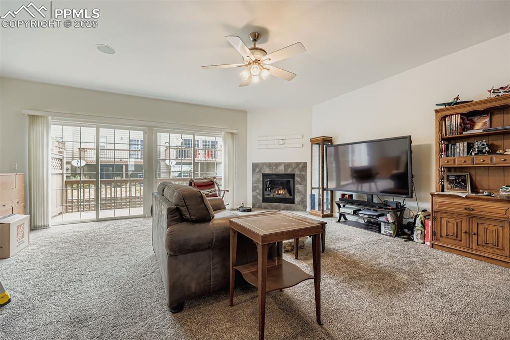 Image 7 of 27: Living area featuring carpet, a tile fireplace, and a ceiling fan