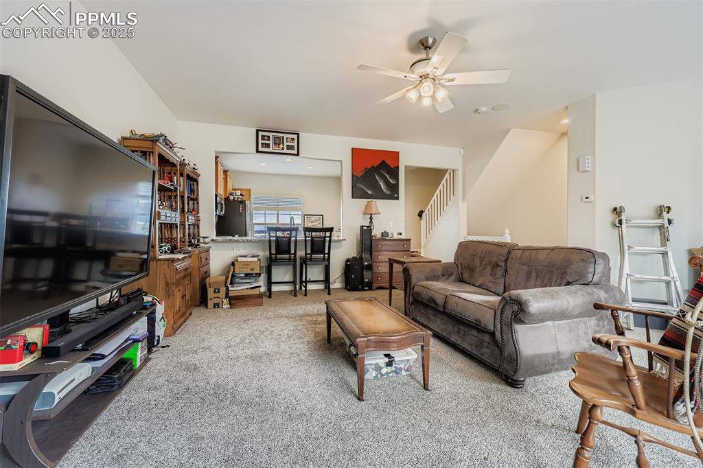 Image 9 of 27: Carpeted living area with stairway and a ceiling fan
