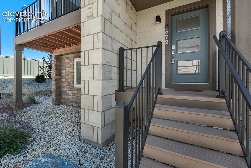 Image 4 of 34: Exterior entryway featuring composite steps, metal railings, stone and bloc