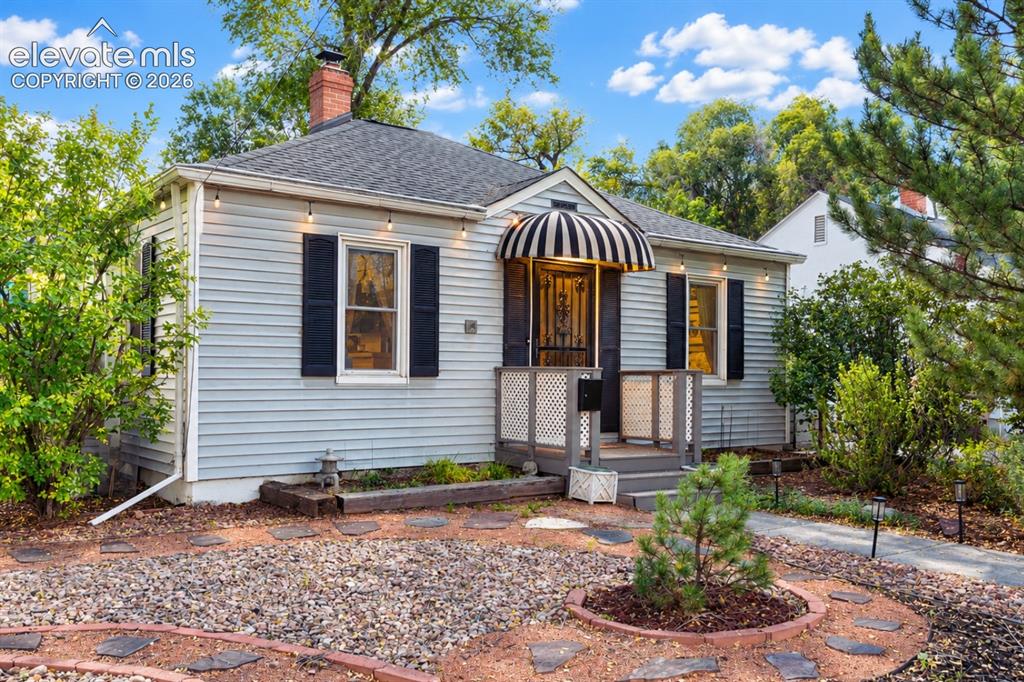Caption: Single-story exterior featuring light-toned horizontal siding, dark window shutters, a decorative st
