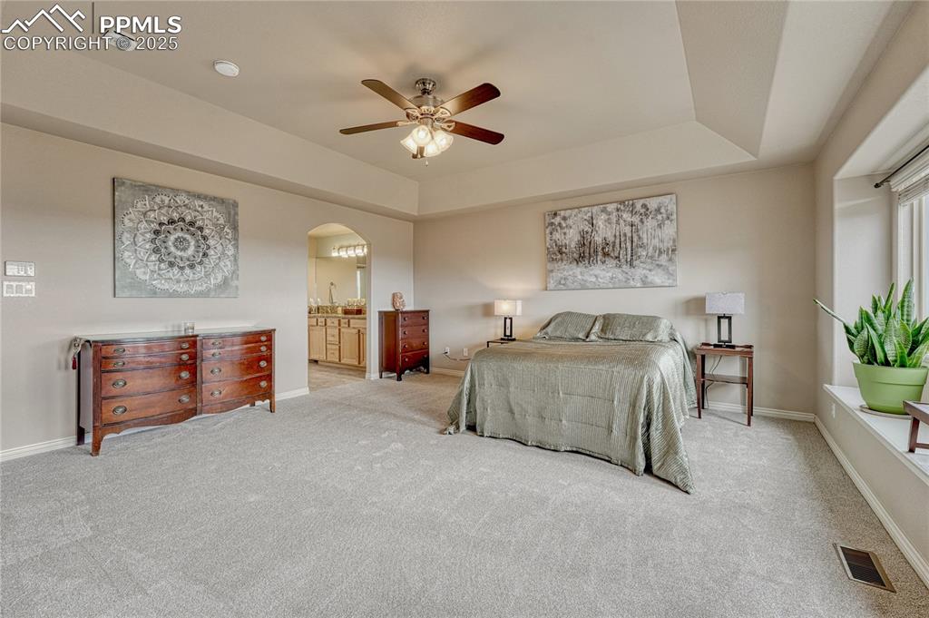 Image 24 of 48: Spacious primary bedroom with window seat, tray ceiling...