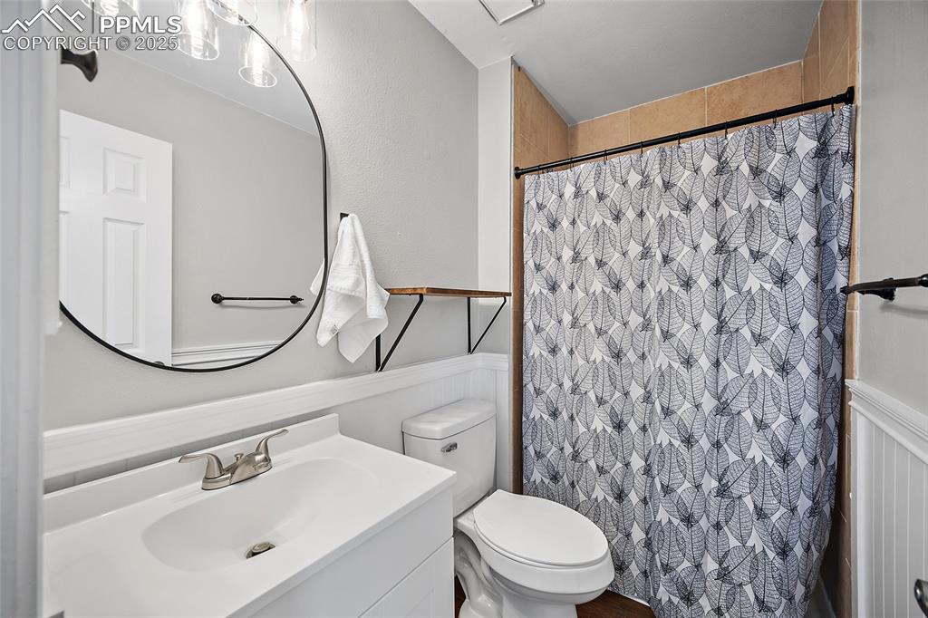 Image 19 of 50: Full bath with a shower with shower curtain, vanity, and a wainscoted wall