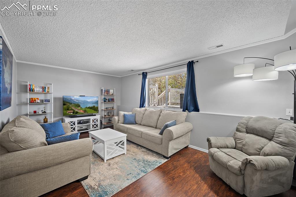 Image 25 of 50: Living area with ornamental molding, wood finished floors, and a textured c