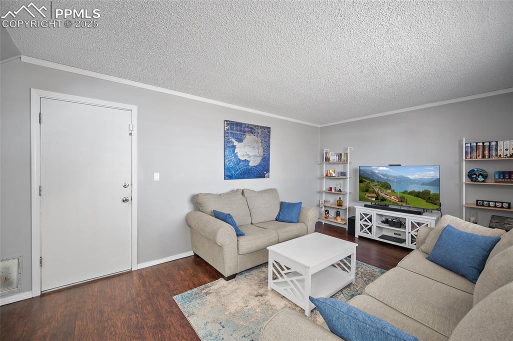 Image 27 of 50: Living area featuring crown molding, dark wood finished floors, and a textu