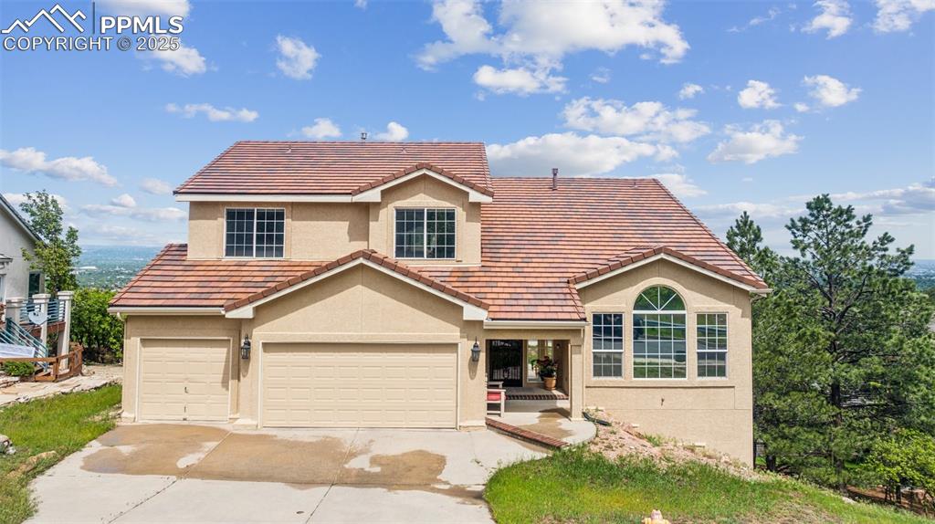 Caption: Traditional-style house featuring stucco siding, driveway, a tile roof, and a garage
