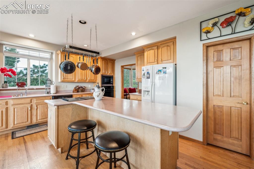 Image 14 of 43: Kitchen featuring a kitchen bar, black appliances, light countertops, light
