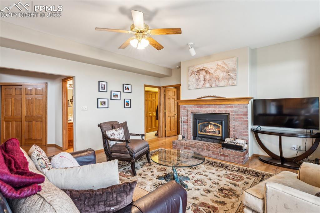 Image 17 of 43: Living area with a fireplace, wood finished floors, and ceiling fan