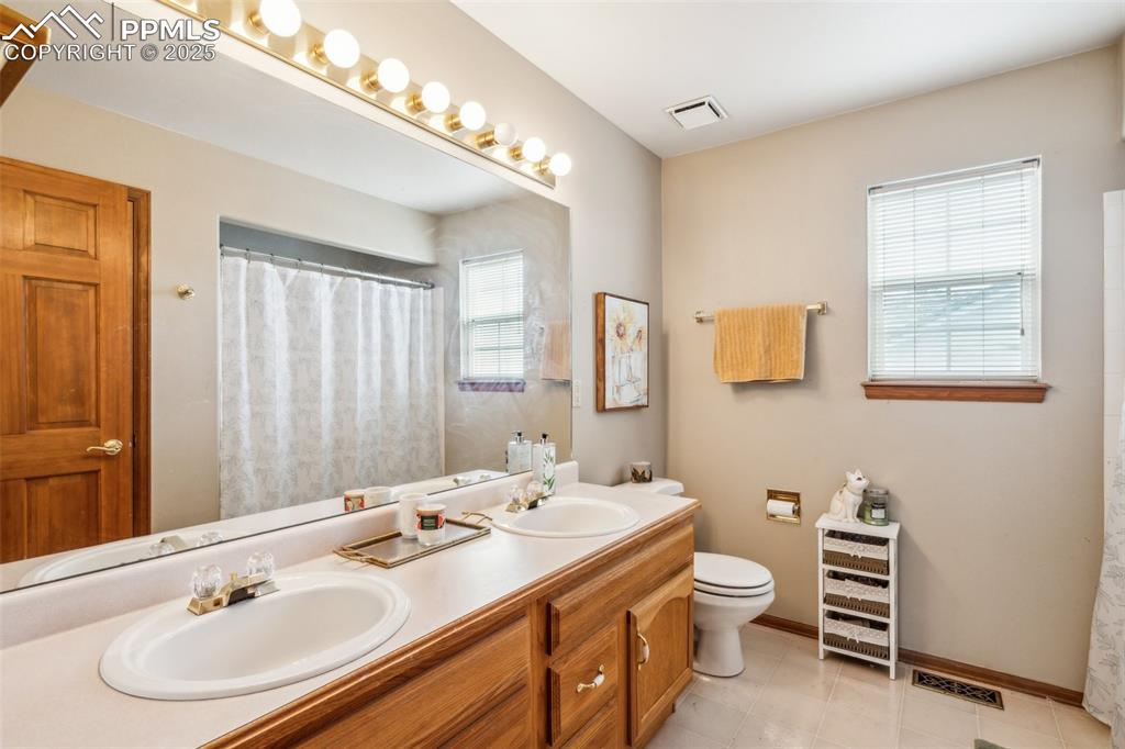 Image 28 of 43: Bathroom with double vanity, light tile patterned floors, and curtained sho