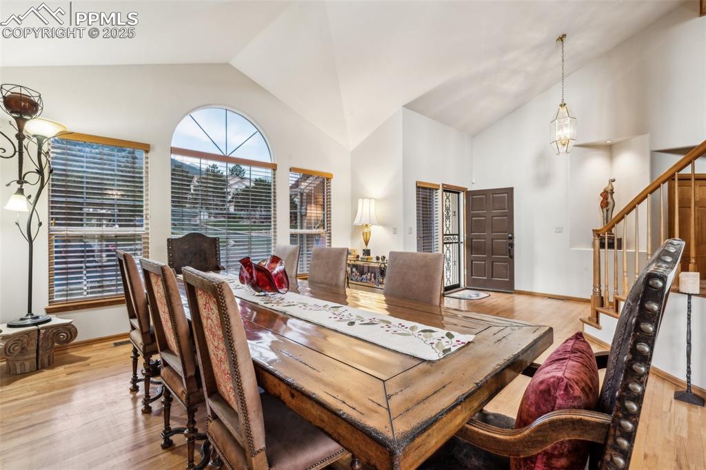 Image 7 of 43: Dining area with stairs, light wood-style floors, and high vaulted ceiling