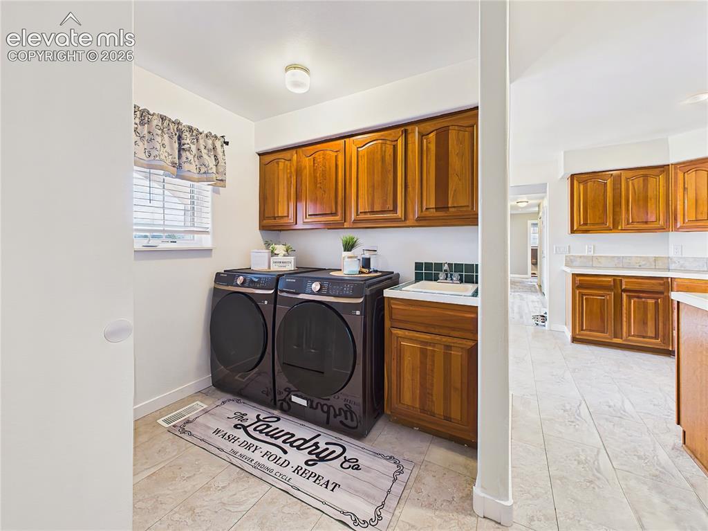 Image 32 of 50: Convenient laundry room features upper cabinetry, utility sink, and dedicat