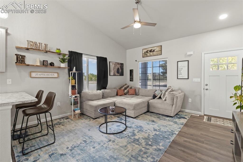 Image 7 of 23: Living area featuring high vaulted ceiling, wood finished floors, and a cei