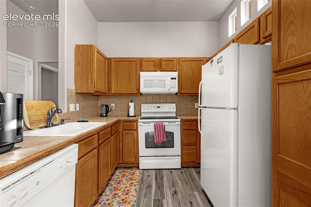 Image 10 of 27: Kitchen featuring wood cabinetry, white appliances, tiled backsplash, dual-