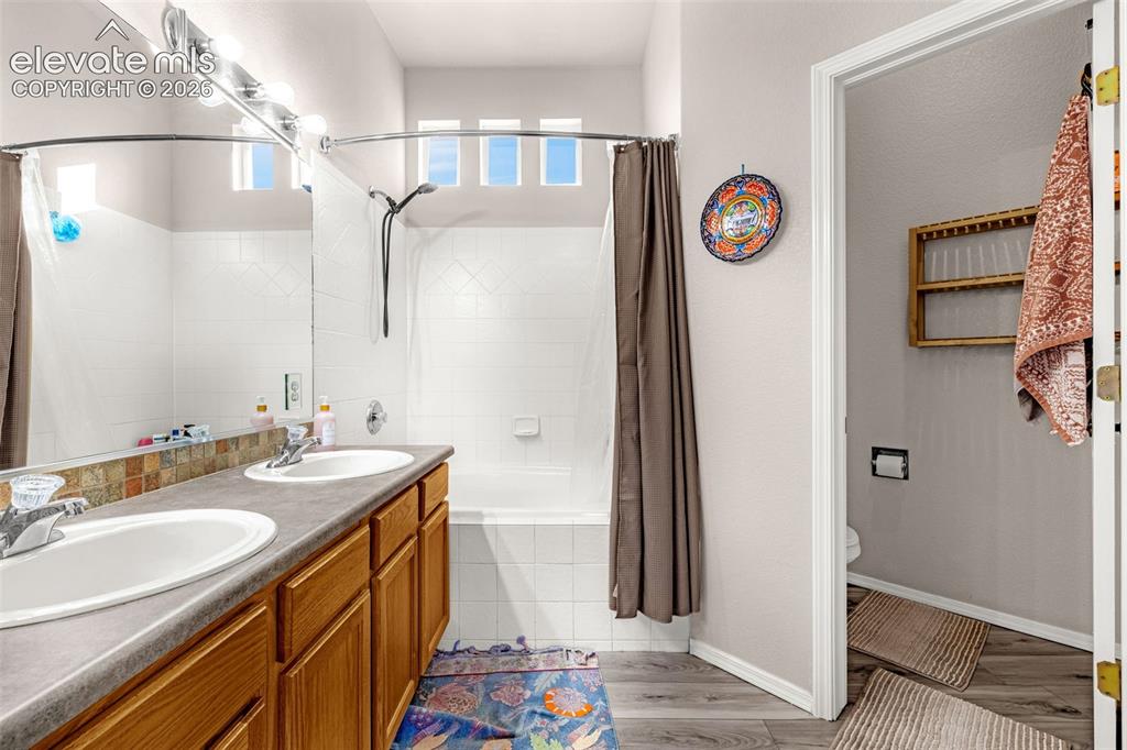 Image 17 of 27: Bathroom featuring a dual-sink vanity with wood-finish cabinetry, a full-wi
