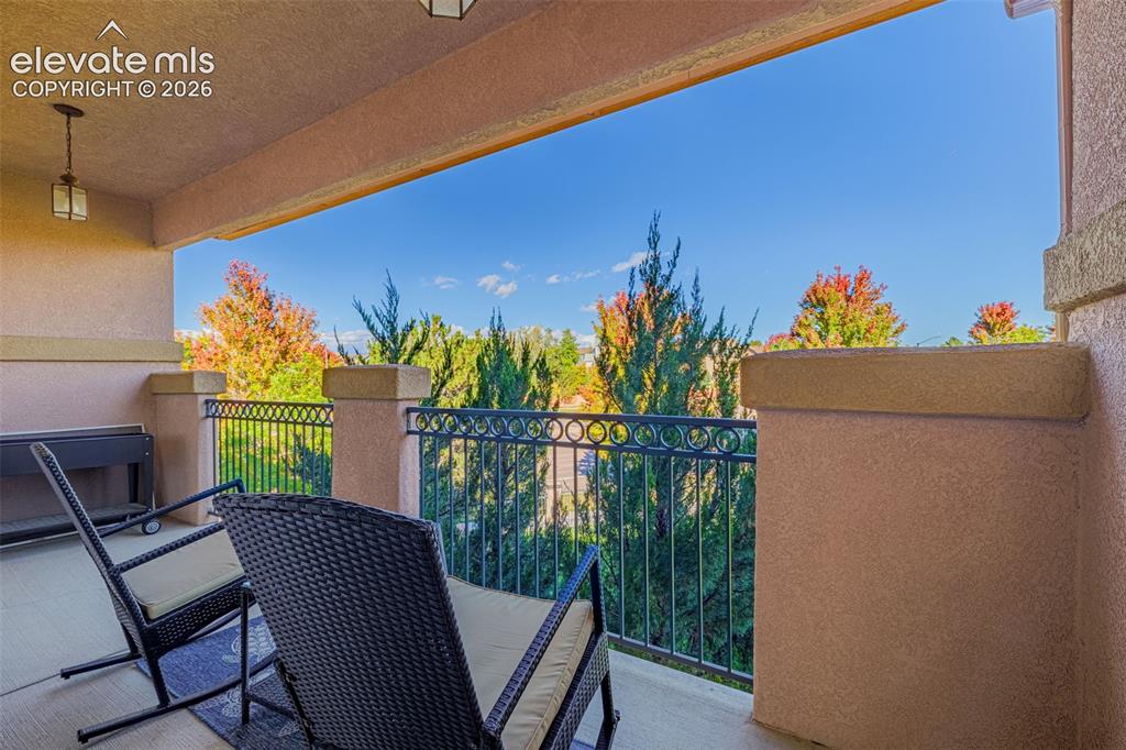 Image 21 of 27: Covered balcony with stucco-finished pillars, decorative metal railing, and