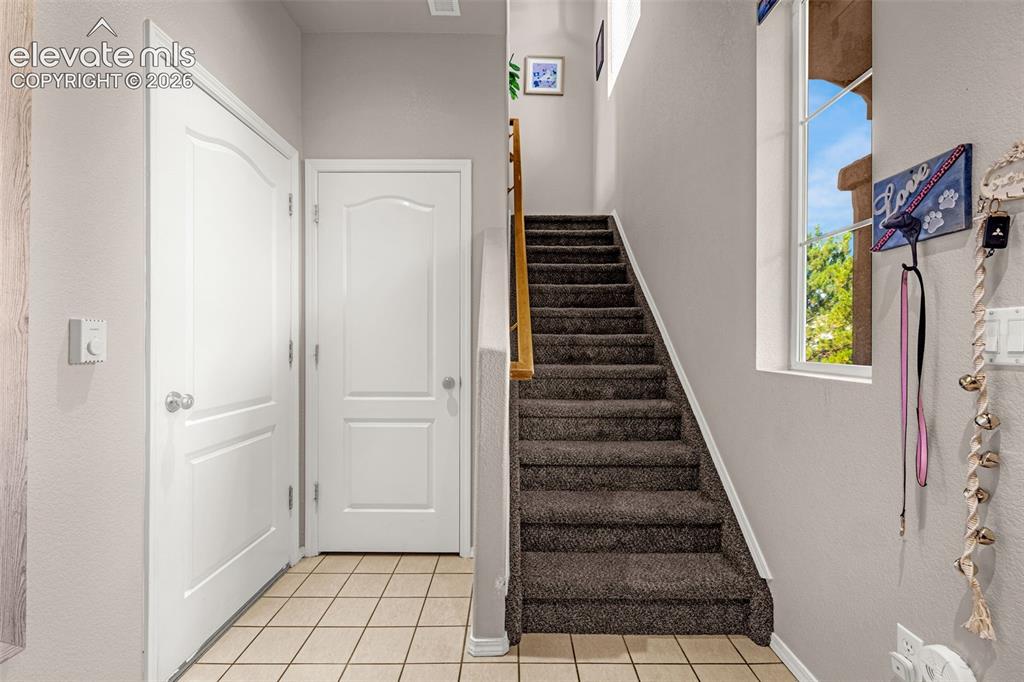 Image 4 of 27: Staircase with plush carpeting and a wooden handrail, tiled flooring, and a