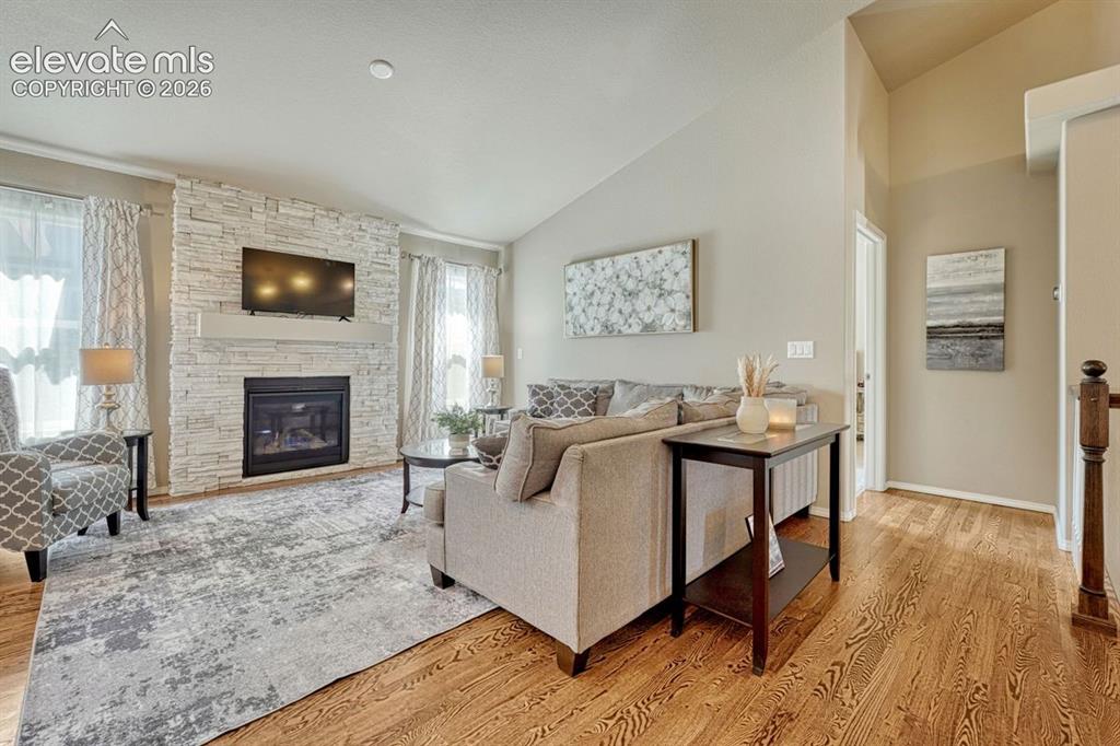 Image 11 of 50: Living room featuring wood flooring, vaulted ceilings, and large windows
