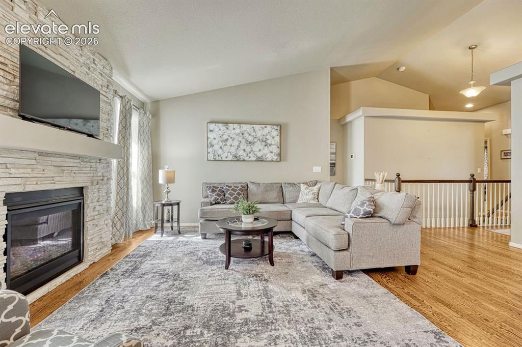 Image 12 of 50: Living area featuring a floor-to-ceiling stacked stone fireplace, vaulted c
