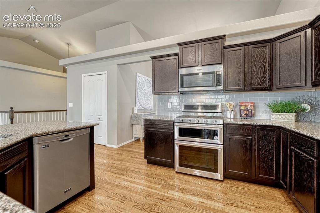 Image 14 of 50: Kitchen featuring dark wood cabinetry, stainless steel appliances, a light-