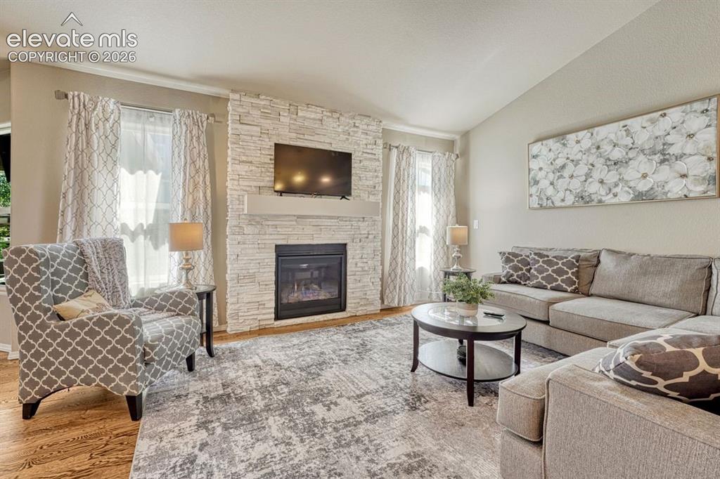 Image 2 of 50: Living room featuring a stacked stone fireplace with a white mantel, vaulte